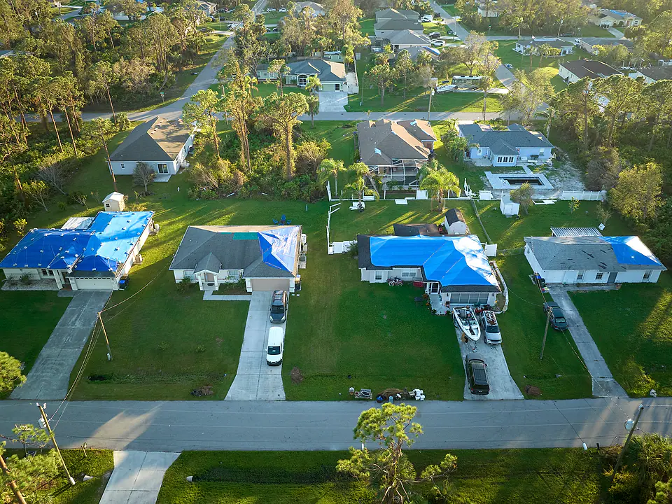 Aerial view of a Florida neighborhood after a storm with several roofs protected by blue tarps